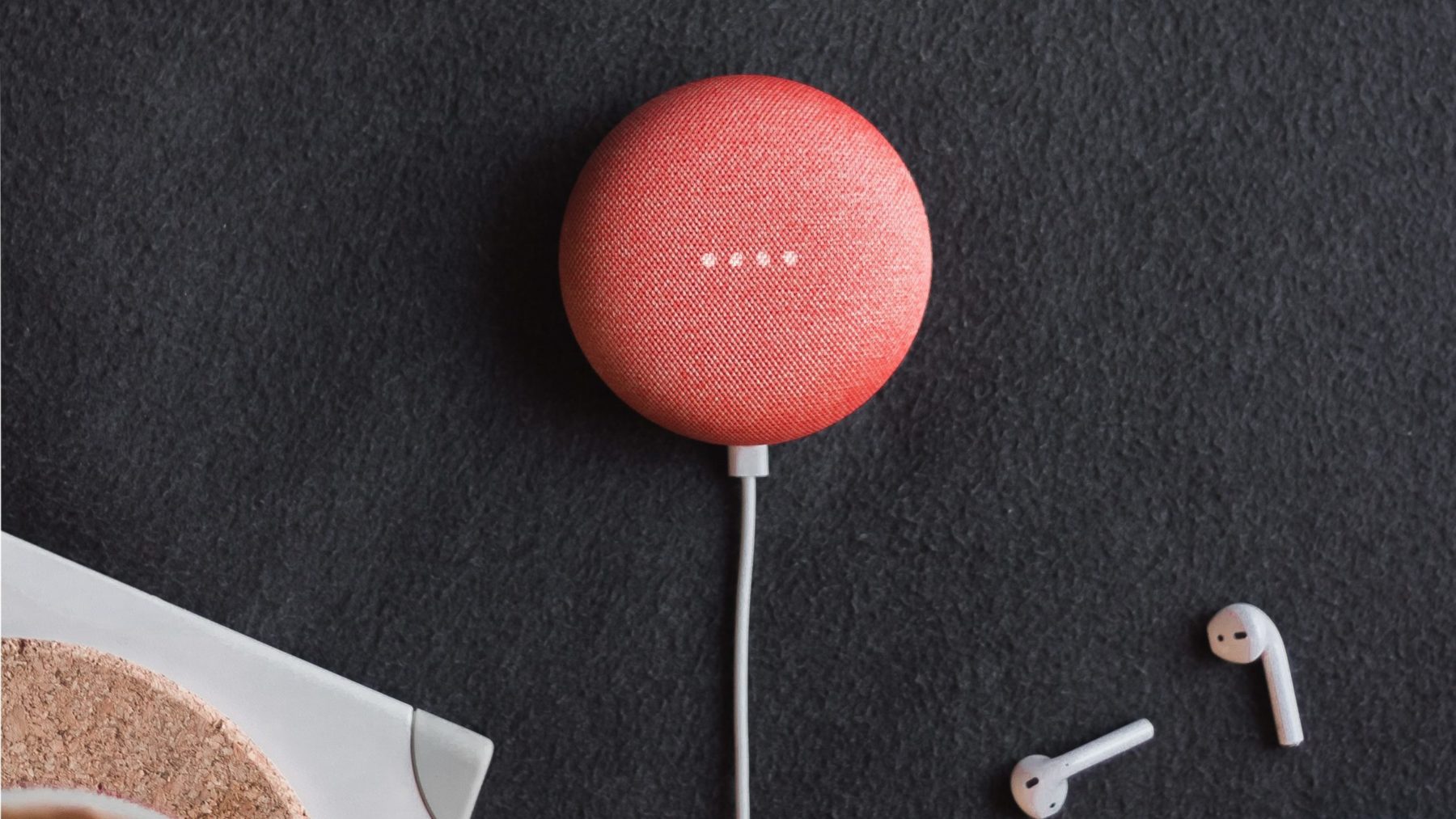 flat lay photography of coral Google Home Mini on black surface beside Apple AirPods